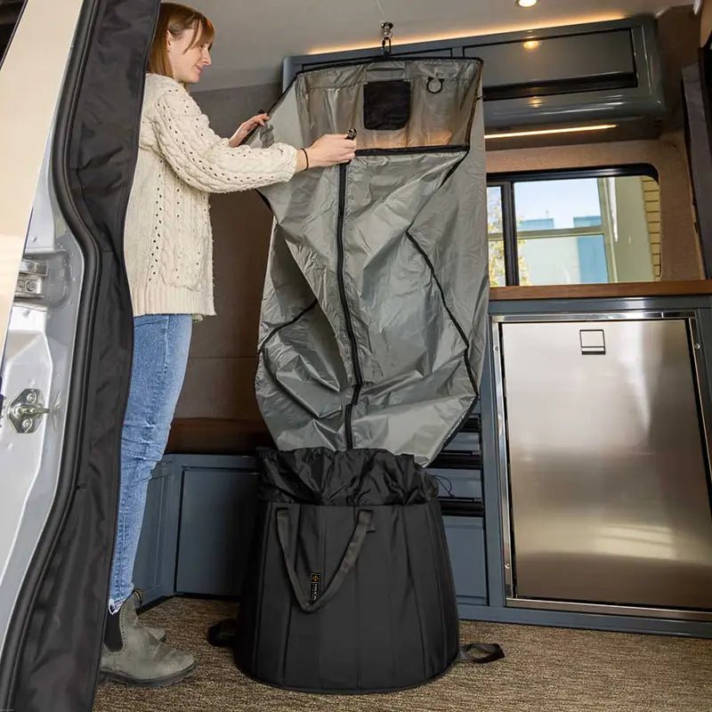 A woman unzipping the portable shower system hanging inside an adventure van.
