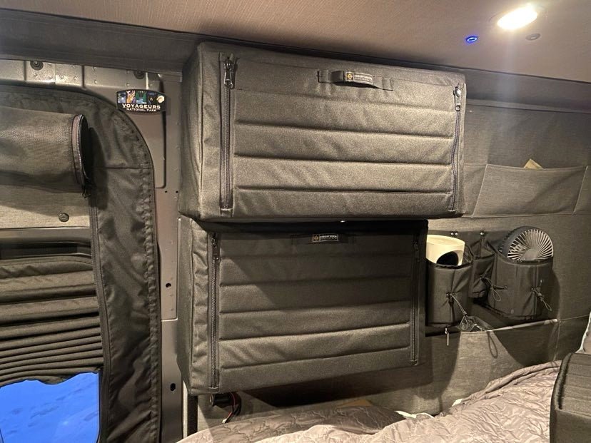 Folded and secured camper van storage cabinets above the bed with fan and organizer pockets nearby