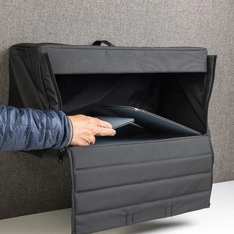 Hand placing tablet inside black wall-mounted van cabinet with zippered drop-down front panel
