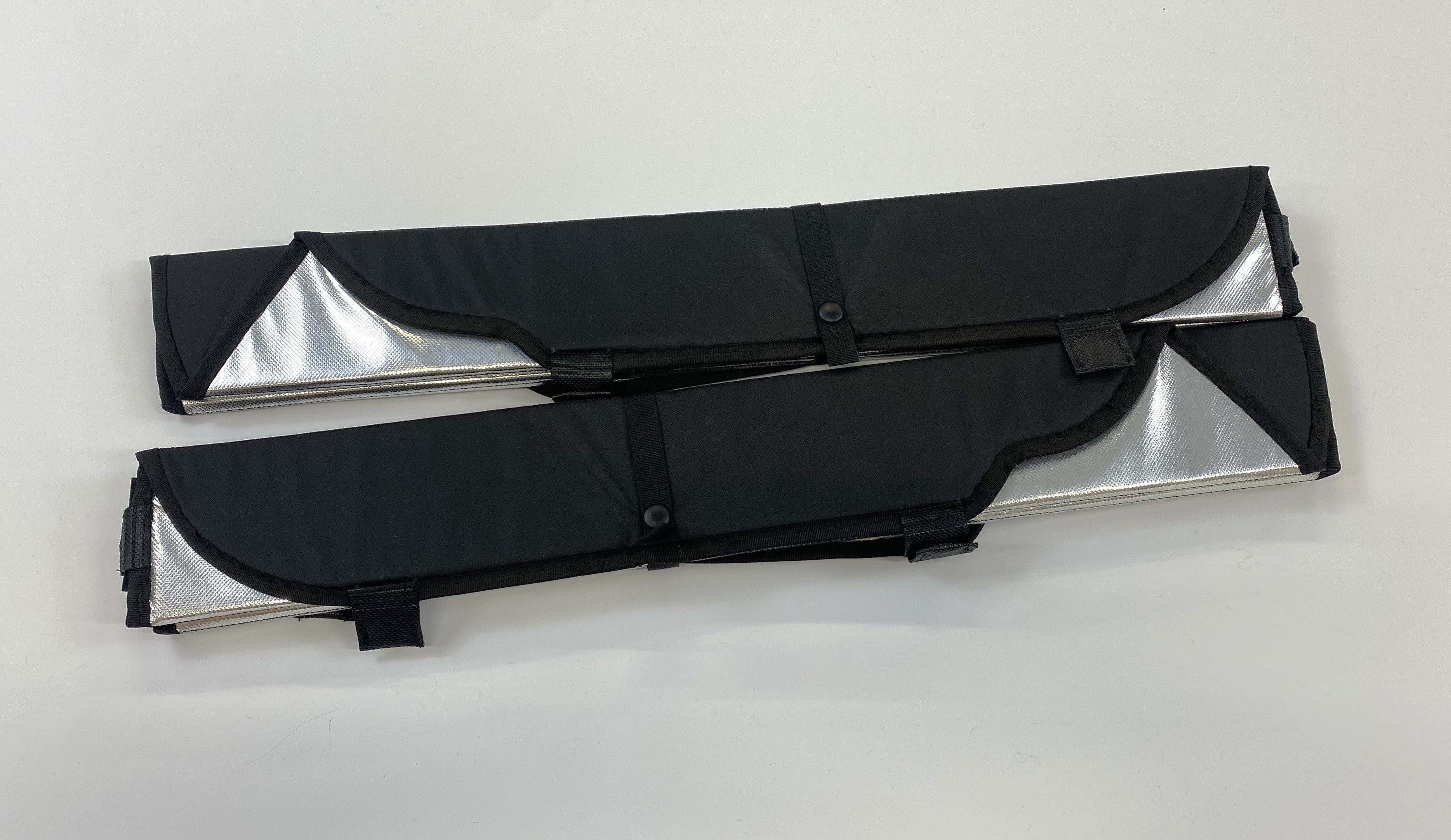 Pair of folded reflective window covers with black fabric exteriors and buttoned straps securing compact storage.