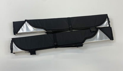 Pair of folded reflective window covers with black fabric exteriors and buttoned straps securing compact storage.