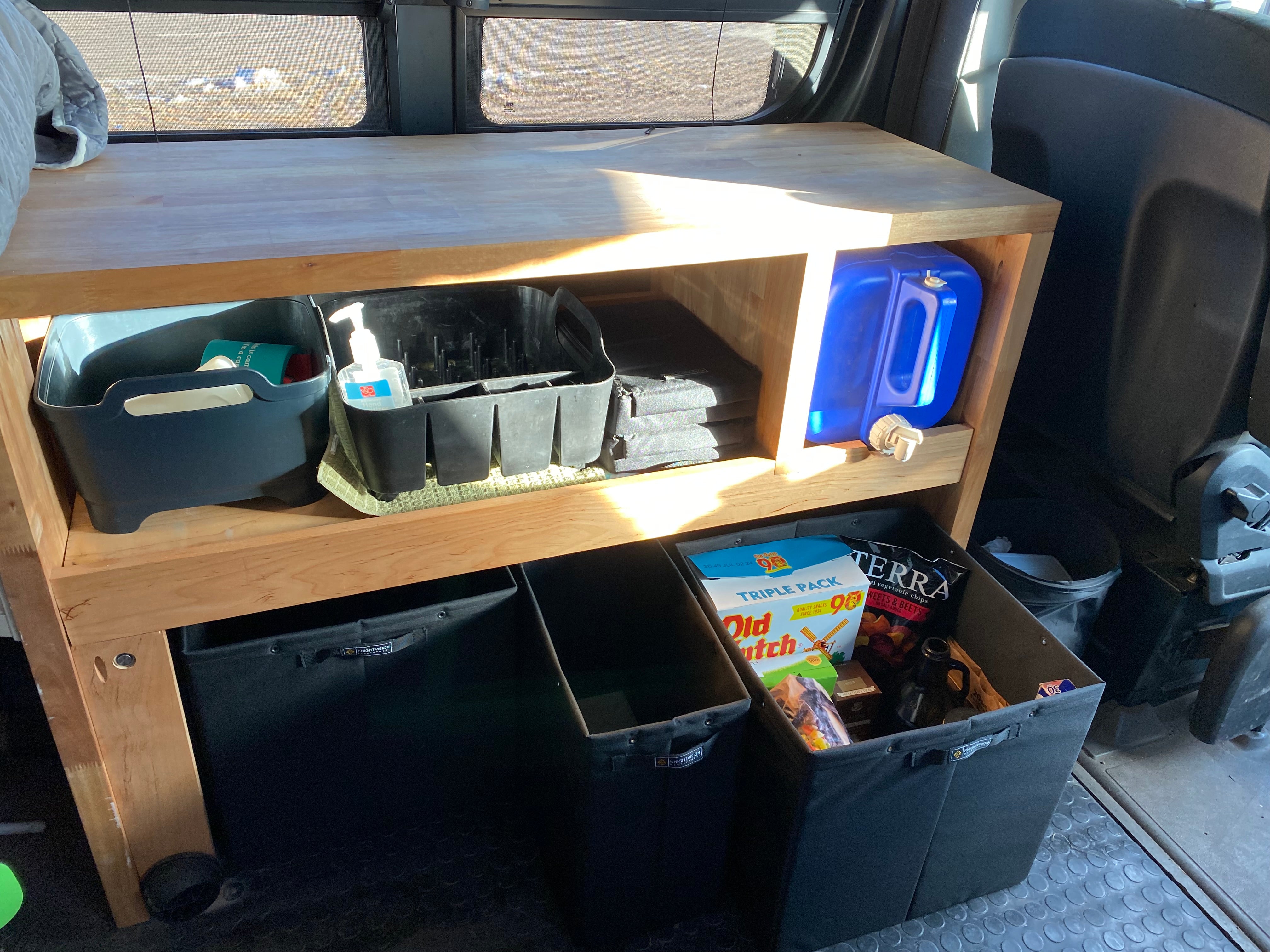 Wooden shelving unit in van with Knight Vision storage bins, snacks, water container, and hygiene items