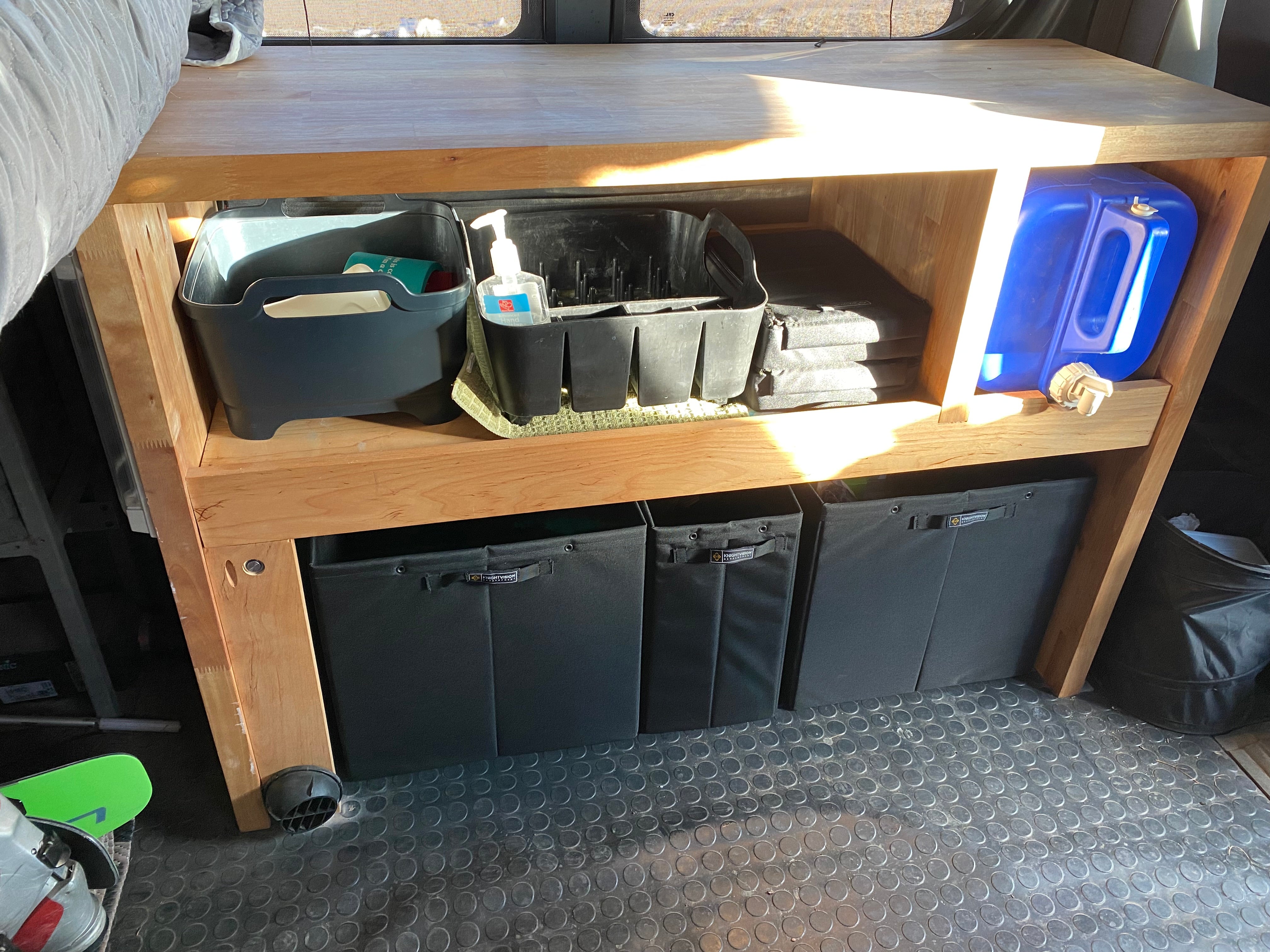 Three Knight Vision storage bins organized neatly under a wooden shelf inside a van setup