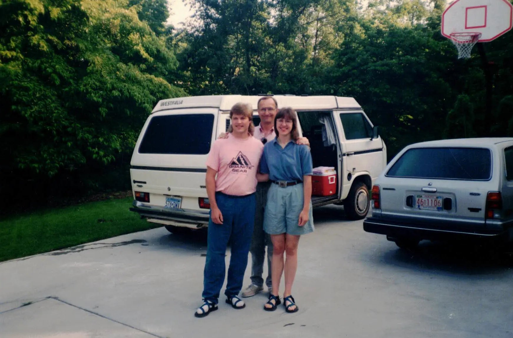 Young Jeff and Lisa Knight pose with a family member in front of their white Volkswagen Westfalia van.