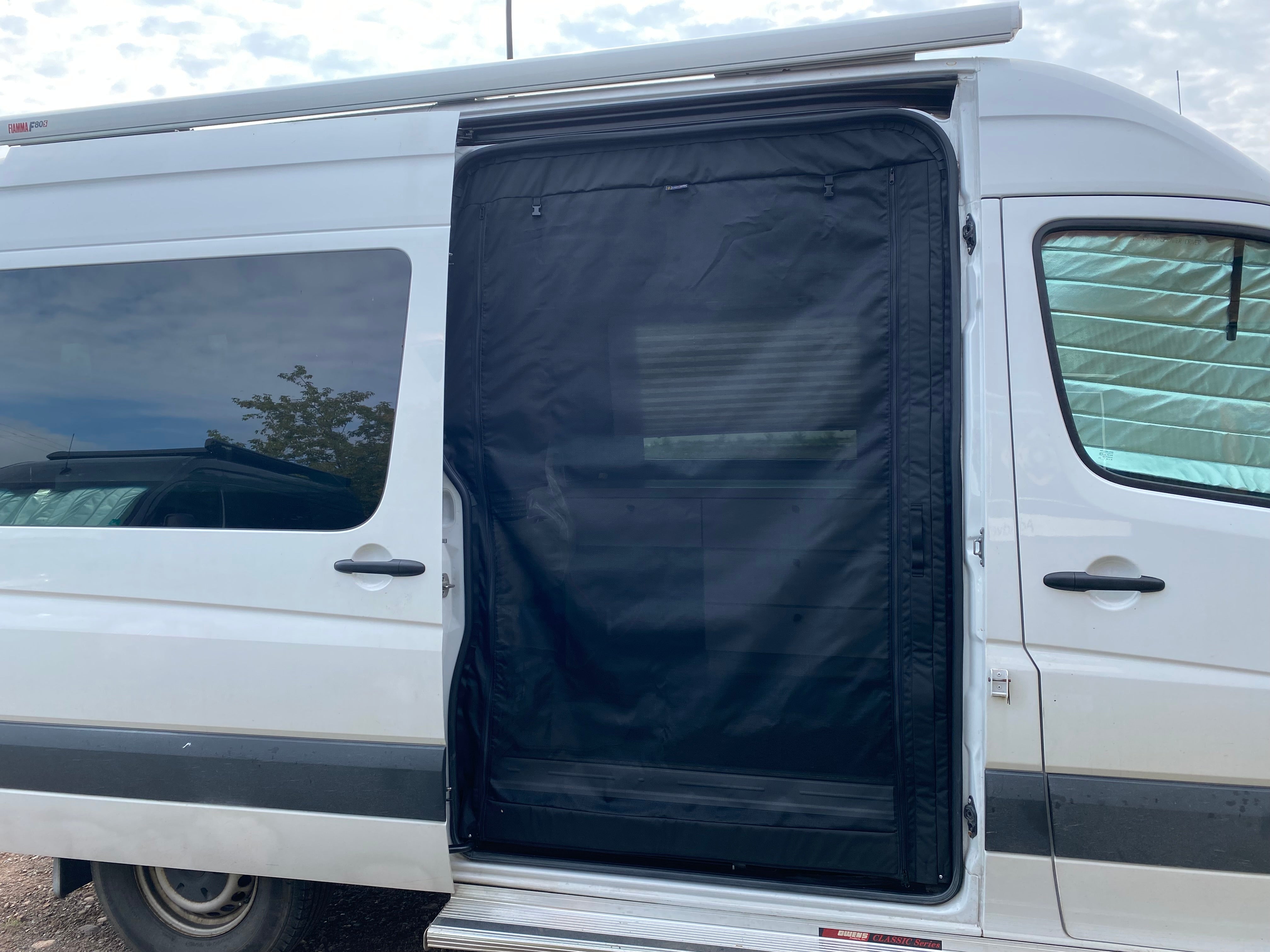 Black bug screen installed in the open sliding door of a white Sprinter van, providing ventilation while keeping insects out.
