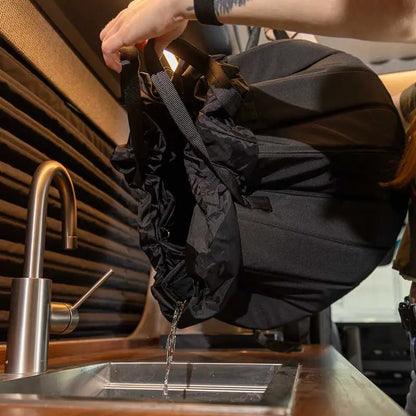 Pouring water from the portable shower system’s basin into a sink inside a camper van.