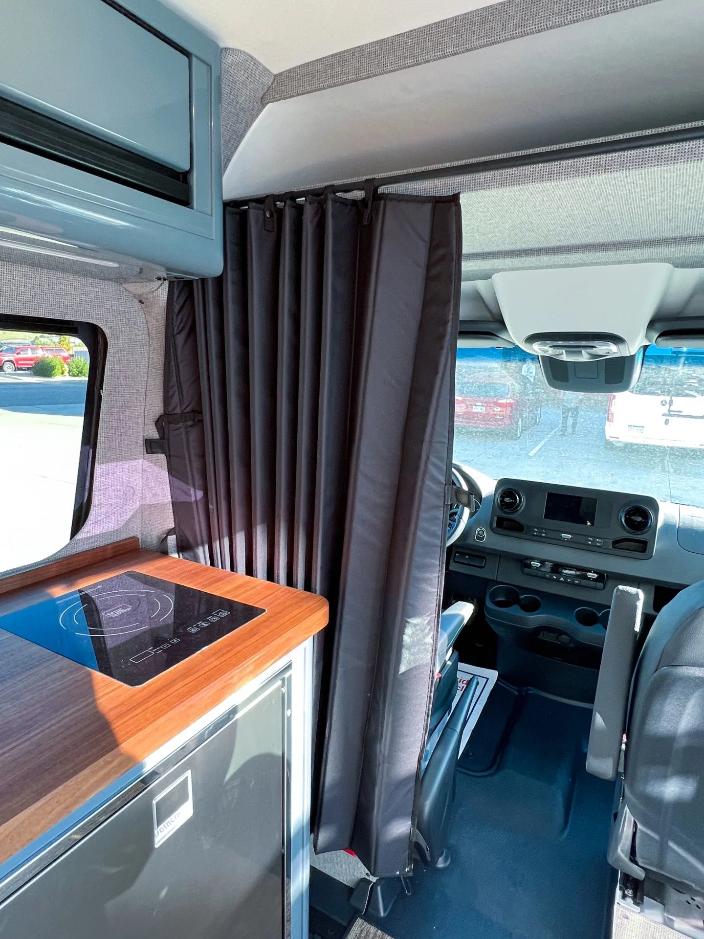 Black privacy cab divider curtain installed behind the front seats of a camper van, separating the cab from the living area.
